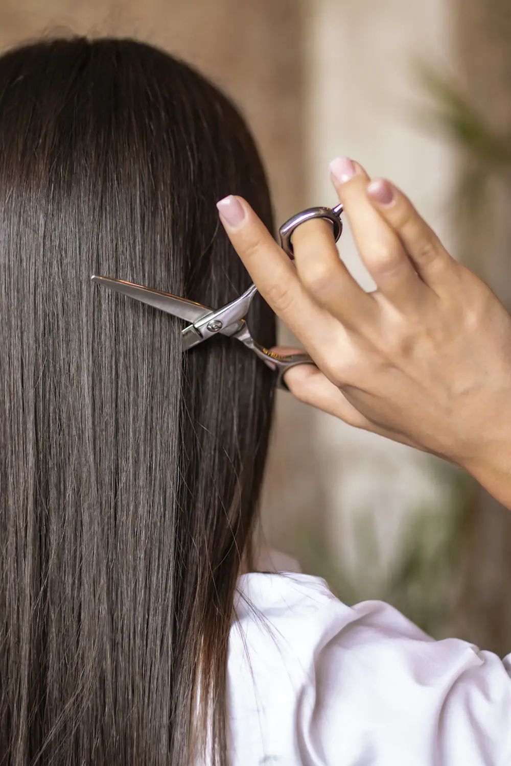 Tesoura cortando uma mecha de cabelo castanho, liso e comprido